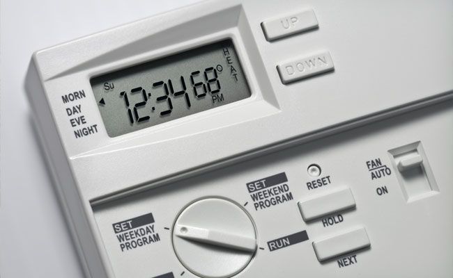 White thermostat with digital display showing the time and temperature. Buttons for programming and fan control.