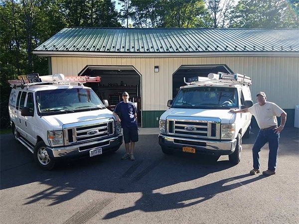 Two white work vans parked outside a garage, two men standing nearby.