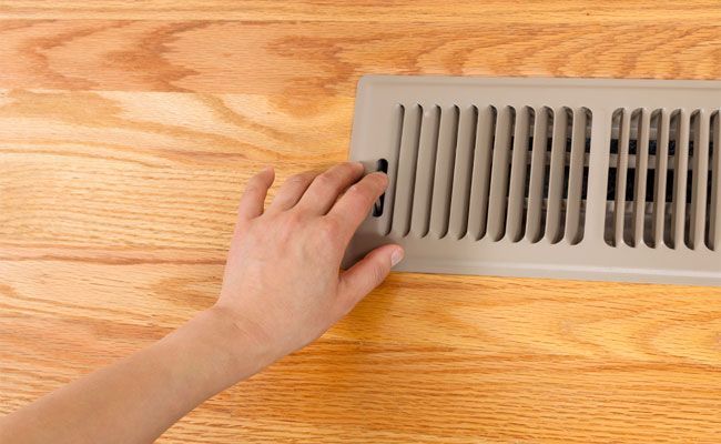 Hand over a floor vent. Beige vent on light wood floor.