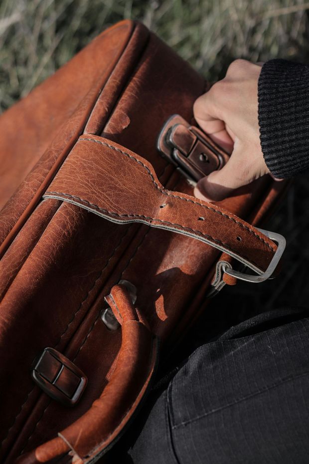 Una mano sujetando el asa de un bolso de cuero marrón al aire libre.