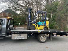 Yellow forklift on a flatbed tow truck; outdoors.