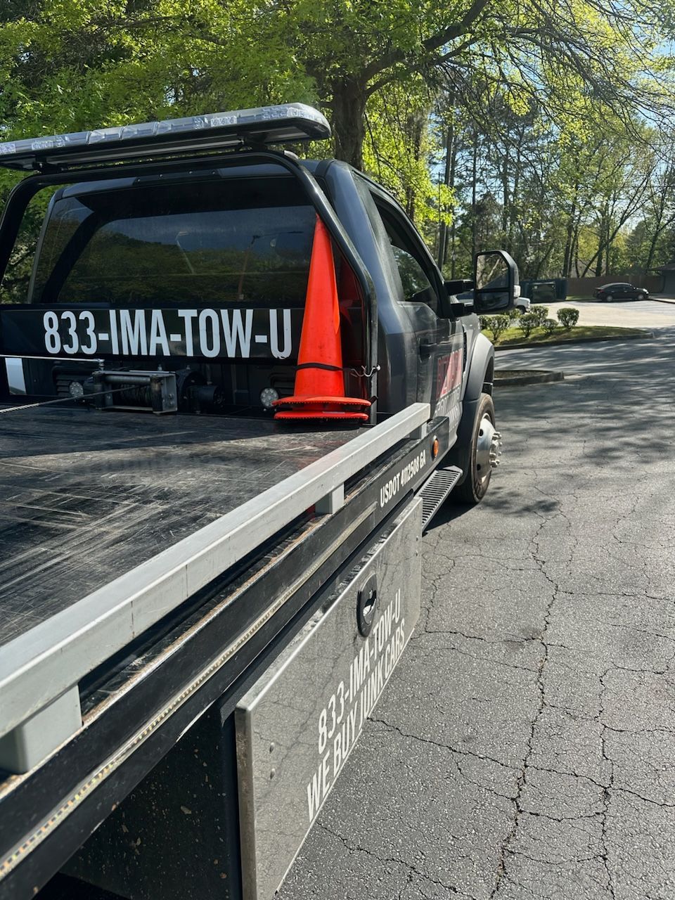 Black tow truck parked on asphalt; orange traffic cone sits on the flatbed.