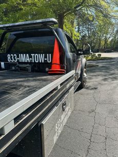Black tow truck parked on asphalt; orange traffic cone sits on the flatbed.