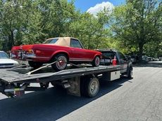 Red convertible on a flatbed tow truck outdoors on a sunny day.