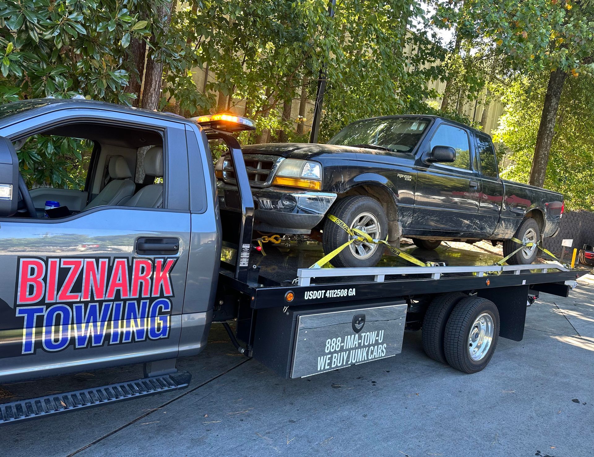 Tow truck hauling a black Ford Ranger pickup truck on a sunny day. 