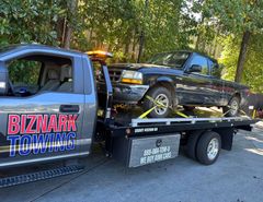 A black Ford Ranger being towed by a Biznark Towing flatbed truck.