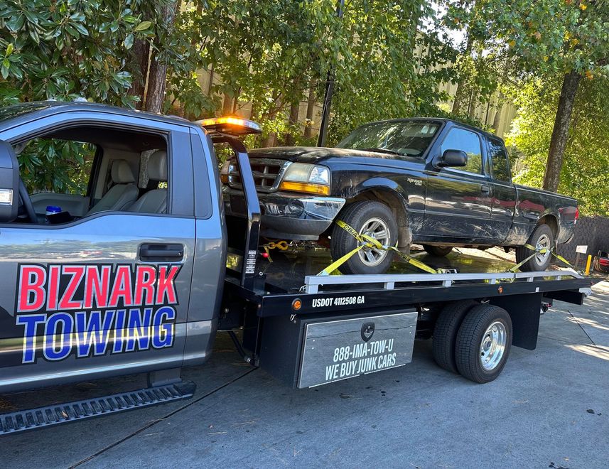 Tow truck hauling a black Ford Ranger pickup truck on a sunny day.