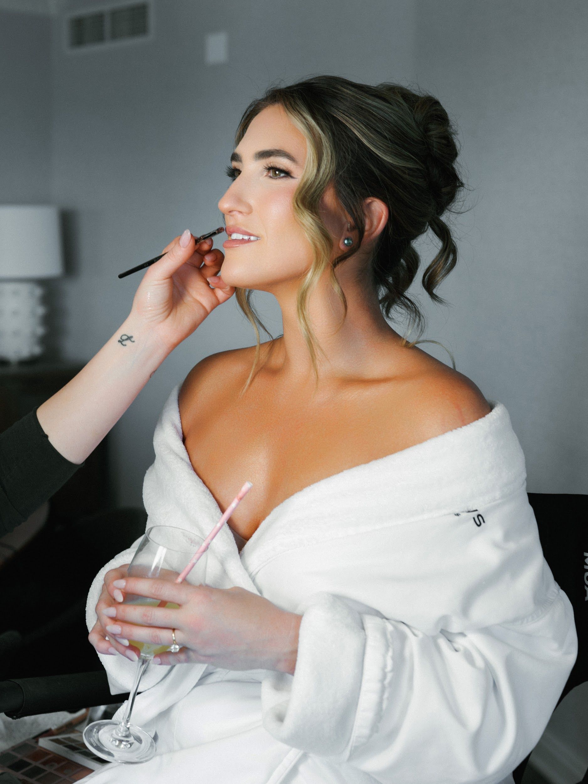 Blonde bride in white off-the-shoulder dress and veil, holding flowers, posed on a deck overlooking ocean cliffs.