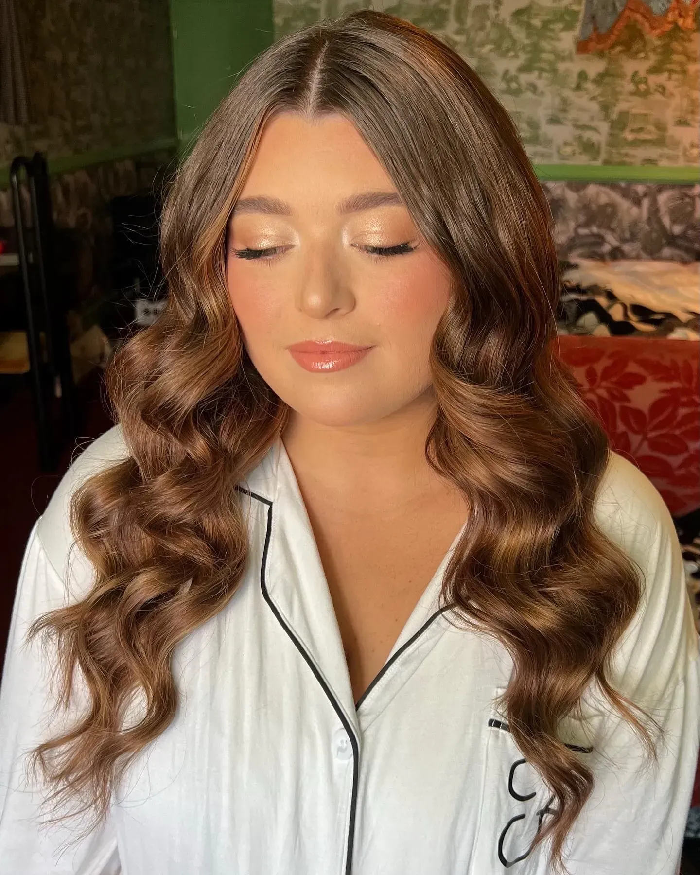 Woman with long, wavy brown hair and soft makeup, wearing a white button-down shirt with black trim.