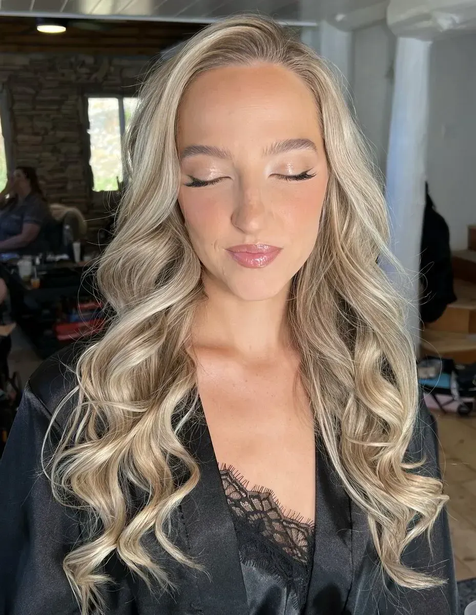 Woman with blonde wavy hair and light makeup, wearing a black robe, eyes closed.