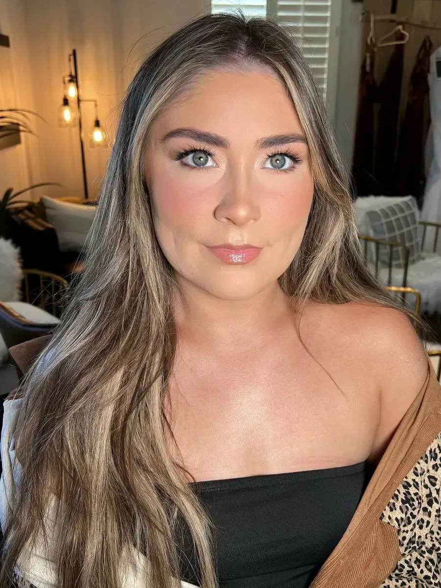 Woman with long, wavy, highlighted hair wearing a black strapless top and patterned jacket, in a well-lit room.