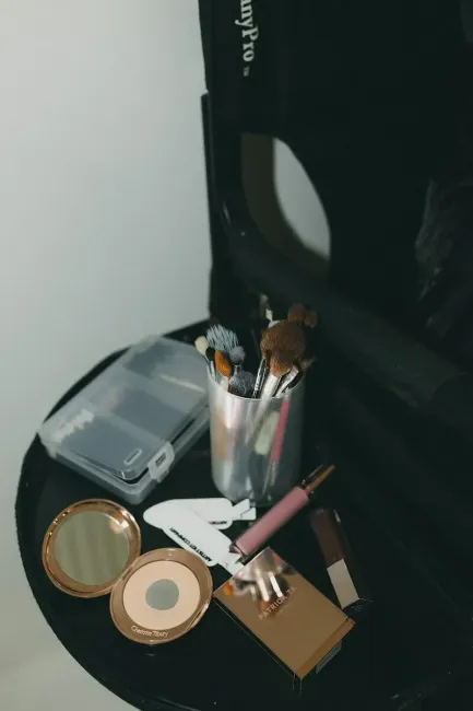 Makeup kit open on a black surface, featuring brushes, a mirror, lip products, and other cosmetics.