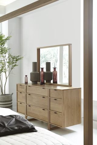 Wooden dresser with mirror, decorated with vases, next to a bed and tree.
