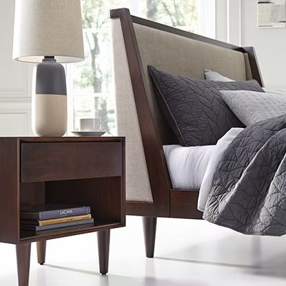 Bedroom with brown nightstand, bed with gray bedding, and a lamp.