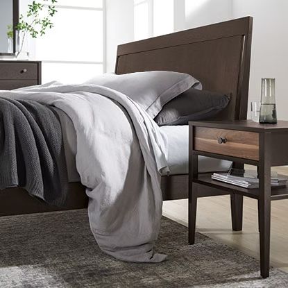 Dark brown bed with gray bedding, a nightstand, and a rug.