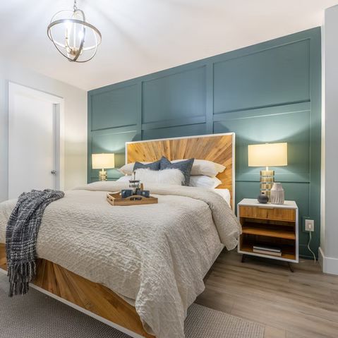 Bedroom with teal accent wall, wooden bed frame, and nightstands, soft bedding, and overhead light.