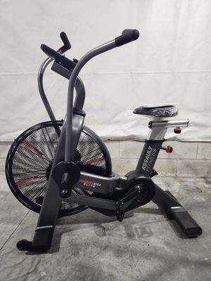 An air bike is sitting on the ground in front of a white wall.