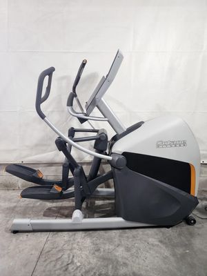 An elliptical machine is sitting on the ground in front of a white wall.