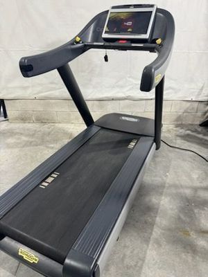 A treadmill with a tablet on top of it is sitting on a concrete floor.