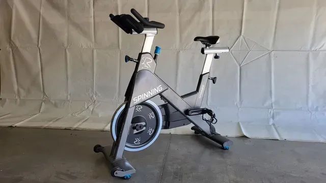 A spinning bike is sitting on a concrete floor in front of a white wall.