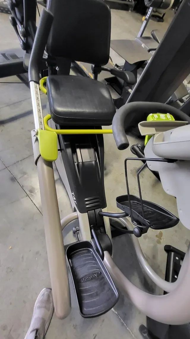 A person is standing next to an exercise bike in a gym.