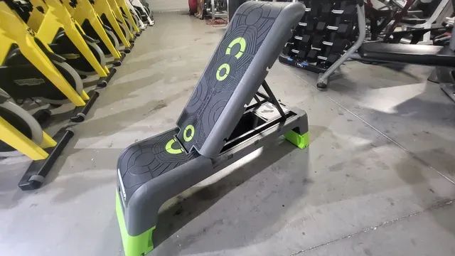 A gray and green bench is sitting in a gym.