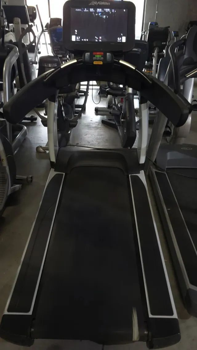 A treadmill with a monitor on top of it in a gym.