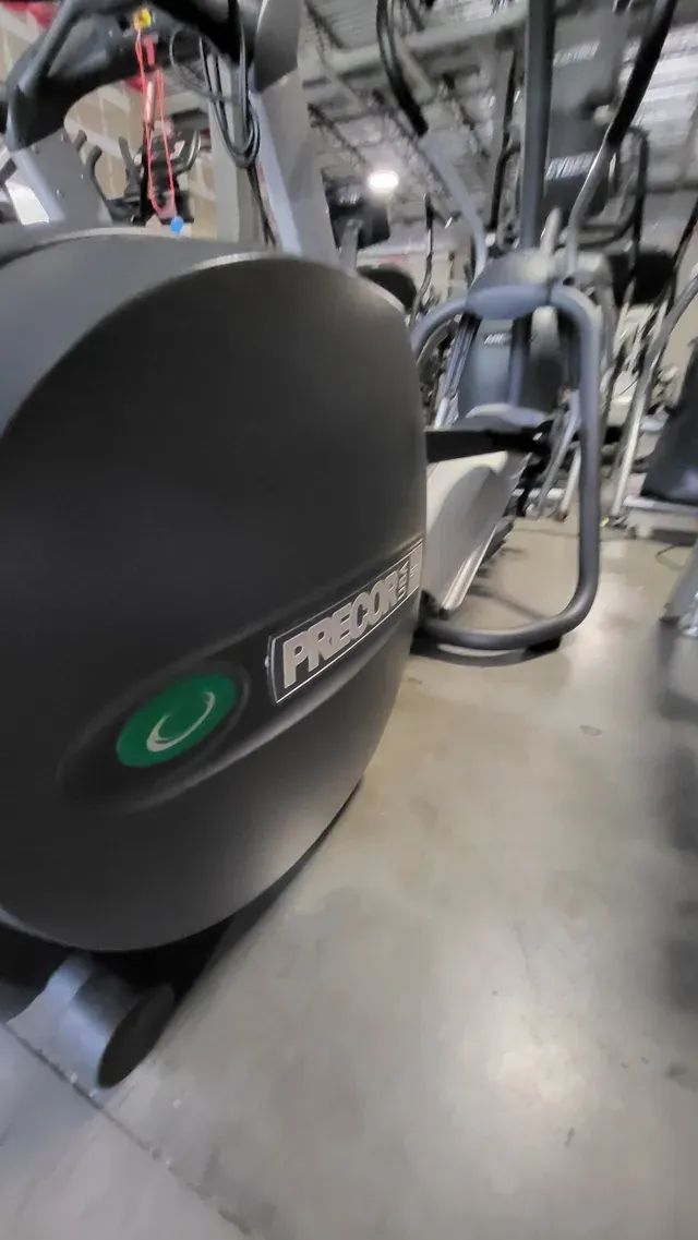 A black elliptical machine is sitting on a concrete floor in a gym.
