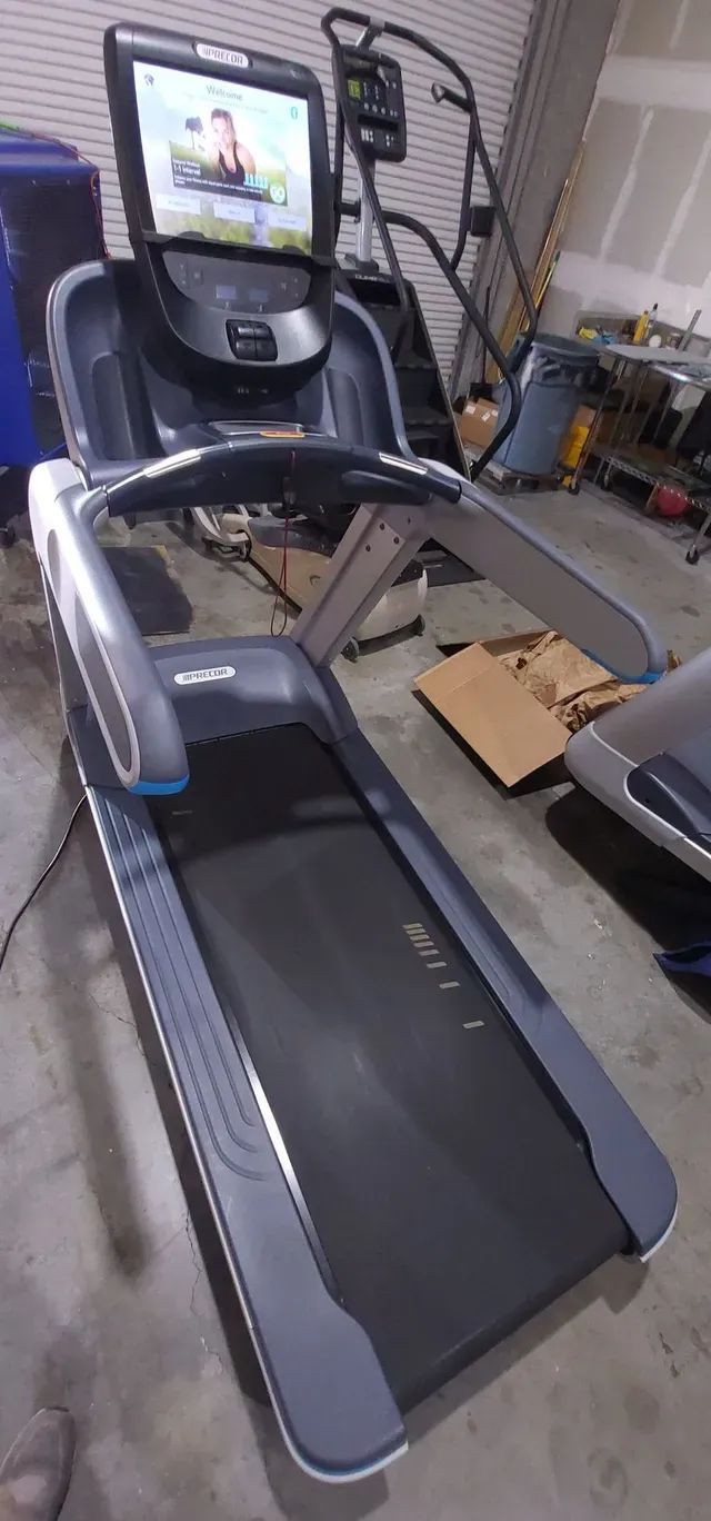 A treadmill with a monitor attached to it is sitting in a garage.
