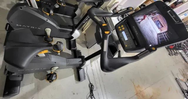 A matrix exercise bike is sitting on a concrete floor in a garage.