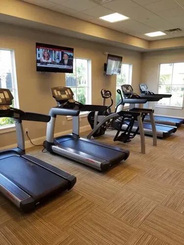 A gym with treadmills , exercise bikes , and a television on the wall.
