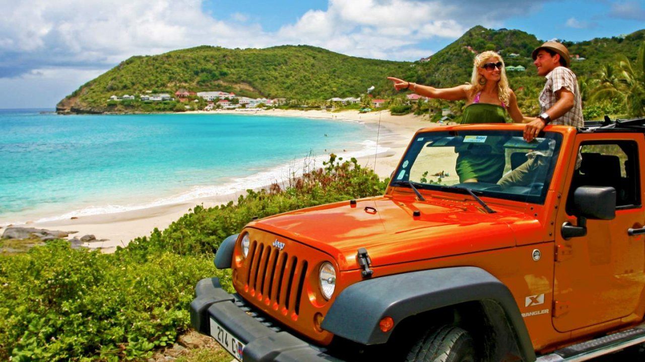A man and a woman are sitting in an orange jeep near a beach.