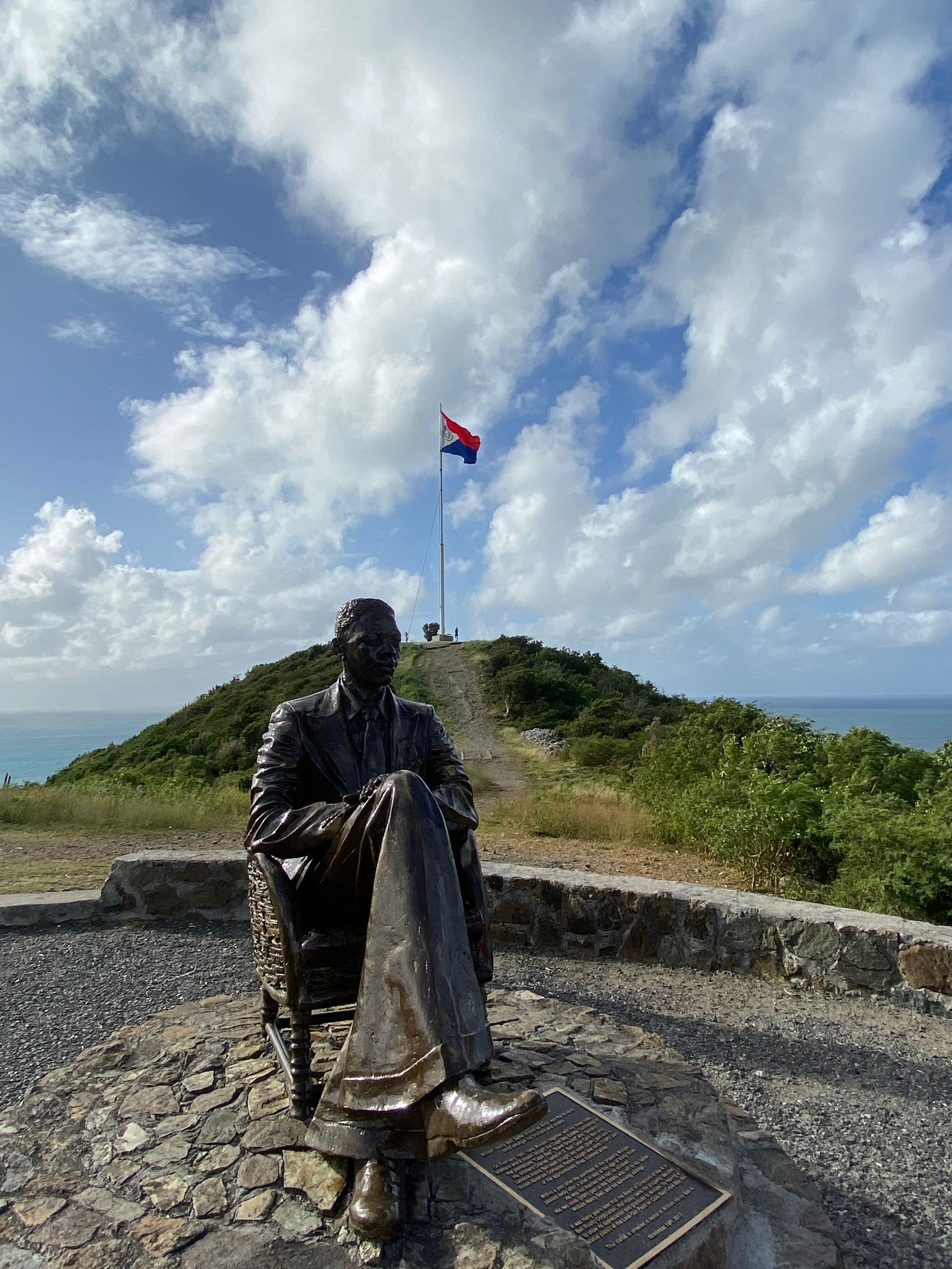 A statue of a man sitting on top of a hill with a flag flying in the background.