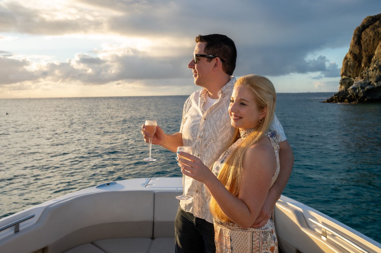 A man and a woman are standing on a boat in the ocean holding wine glasses.