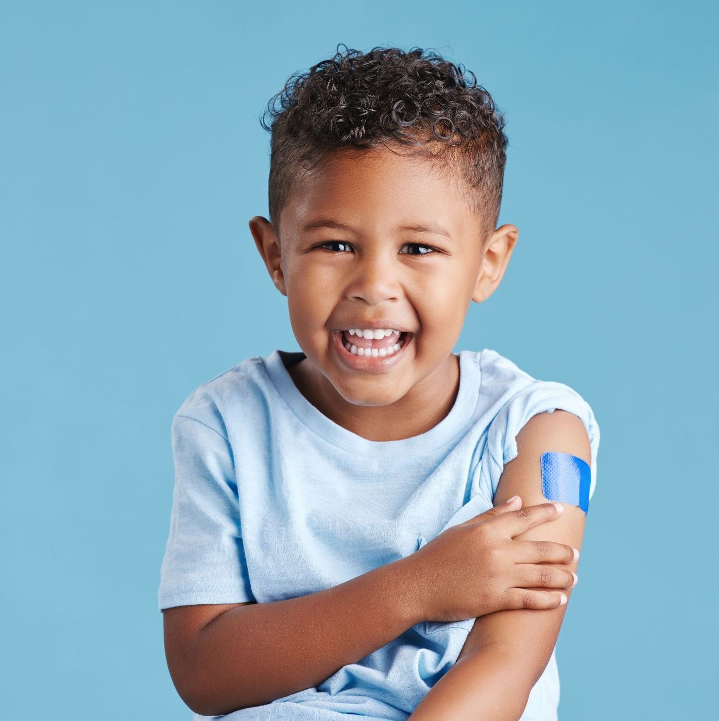 smiling young child showing band-aid on arm after vaccination