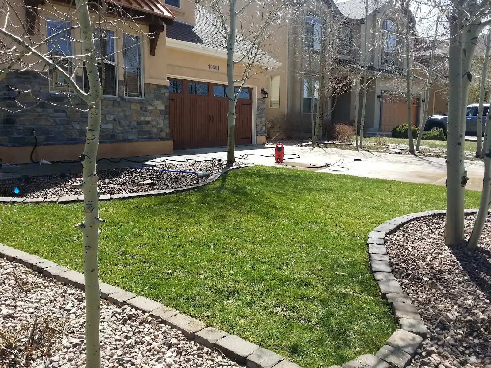 Landscaped apartment courtyard with green lawn, curved stone borders, trees, and a fire hydrant in sunlight