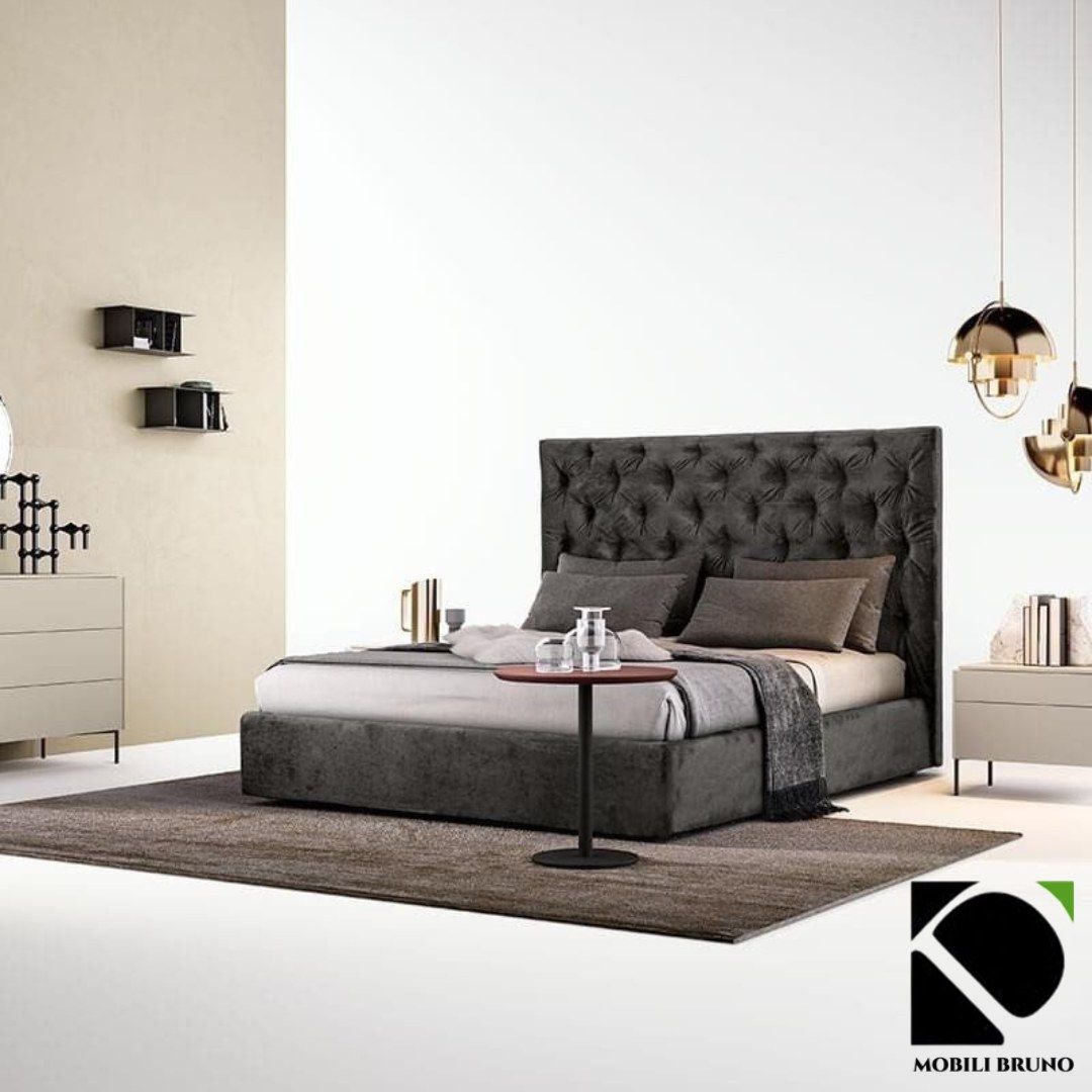 Camera da letto con letto grigio trapuntato, comodini e lampade a sospensione.