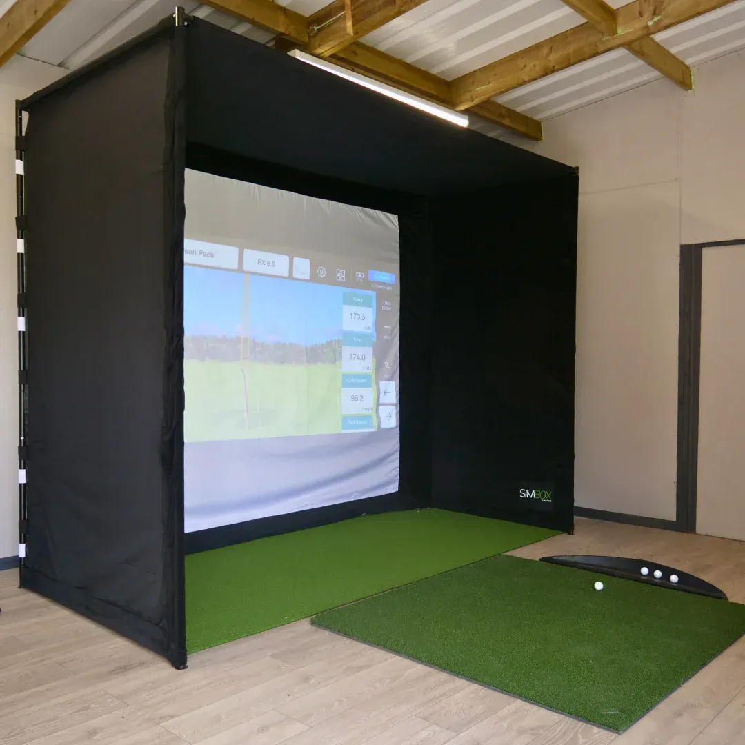Golf simulator with black enclosure, green turf, and projected screen displaying a golf course.