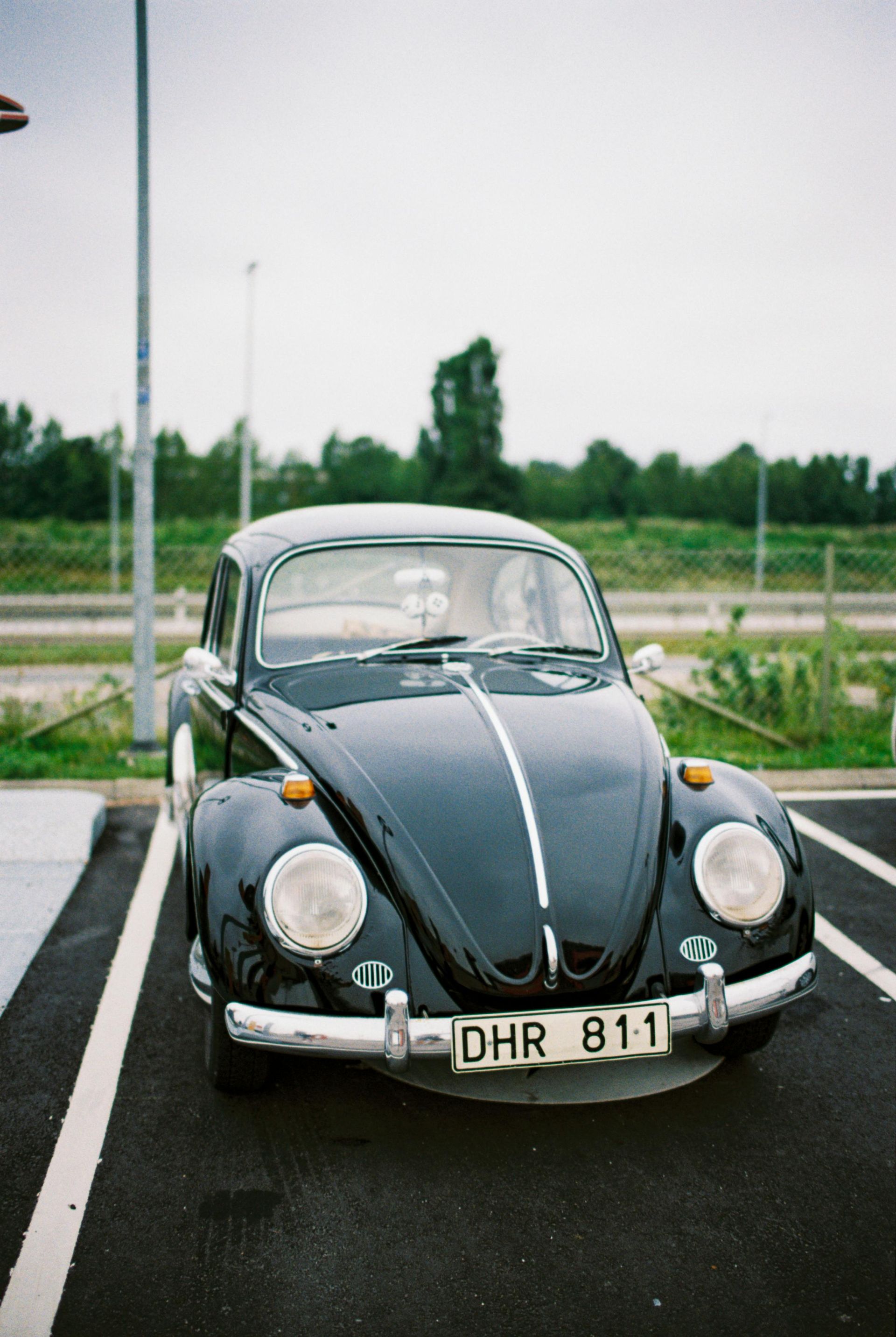 Black vintage Volkswagen Beetle parked in a parking lot on an overcast day.