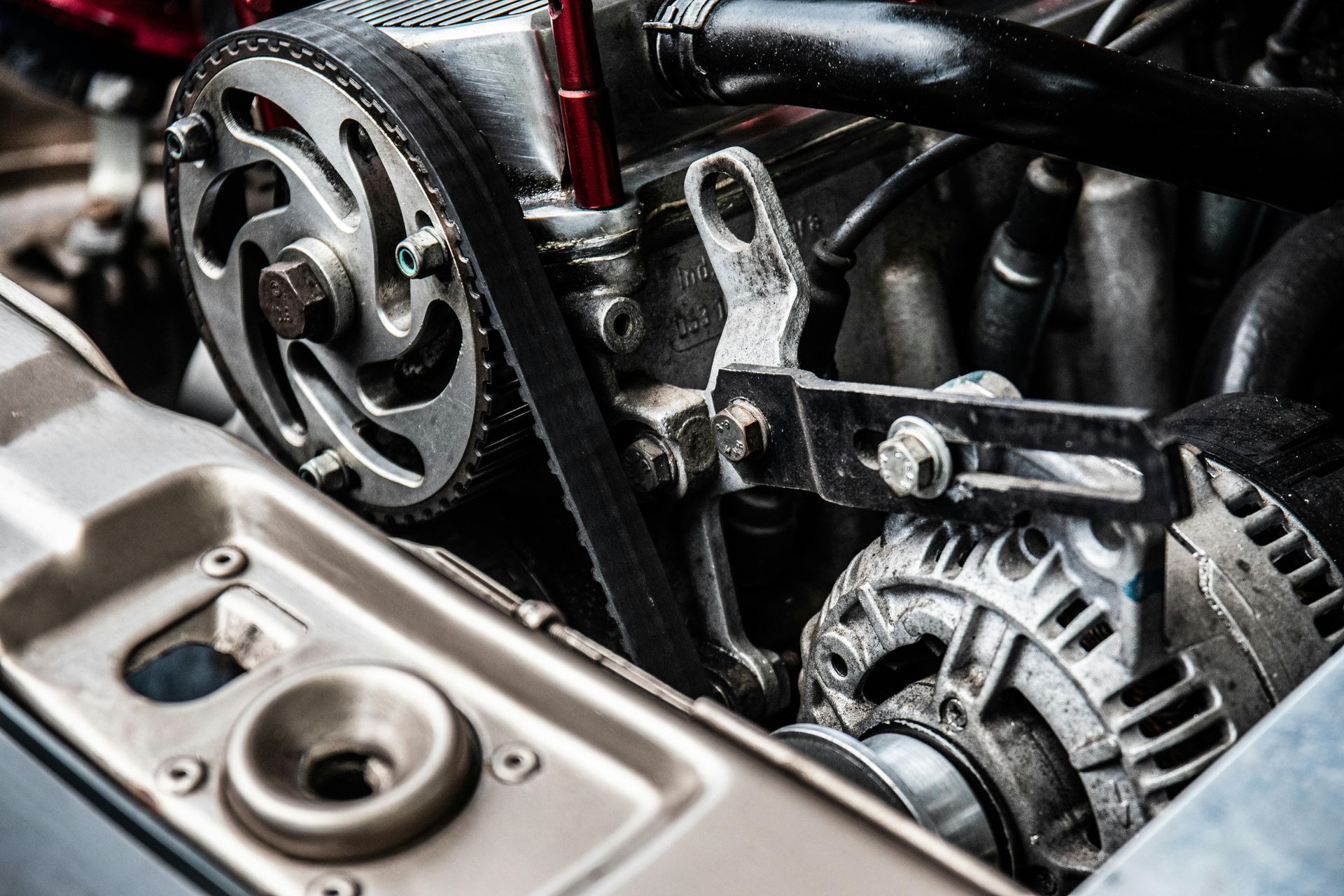 Close-up of an engine's timing belt, pulleys, and alternator. Metallic and black components in an automobile.