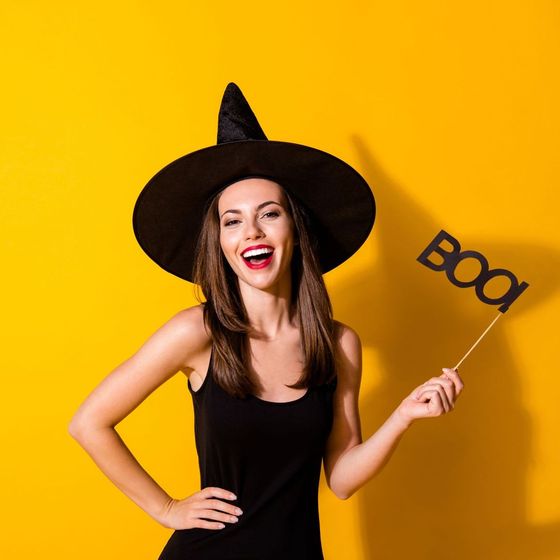 A woman in a witch hat is holding a boo sign