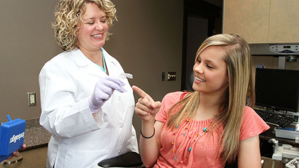 A woman is sitting in a dental chair talking to a dentist.