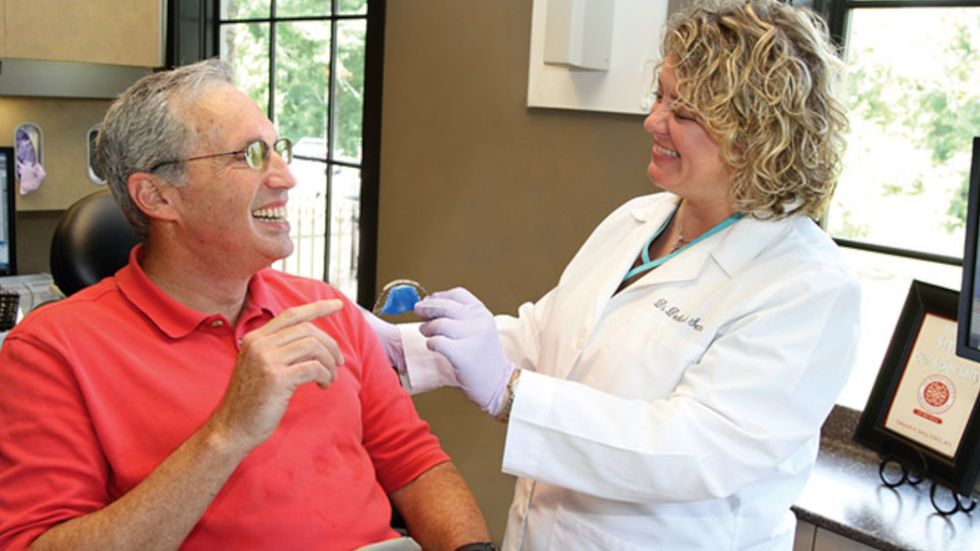 A man is sitting in a dental chair talking to a female dentist.