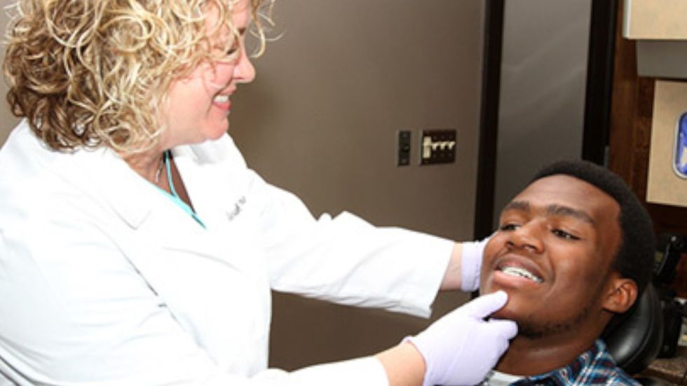 A woman is examining a man 's teeth in a dental office.