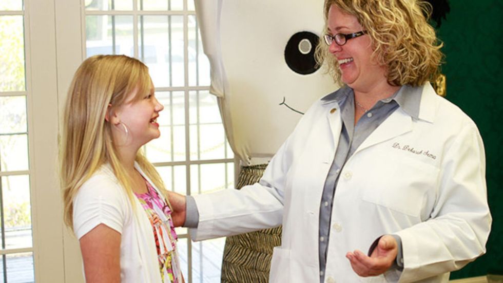 A woman in a white coat is talking to a young girl.