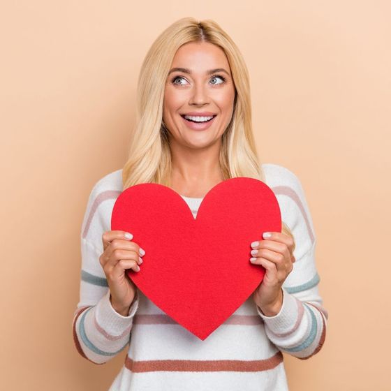 A woman is holding a red heart in her hands.