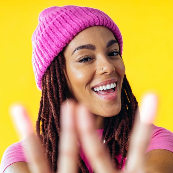 A woman with dreadlocks is wearing a pink hat and smiling.