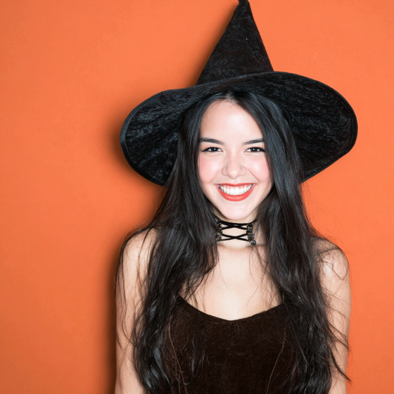 Woman in witch hat smiling against orange background.