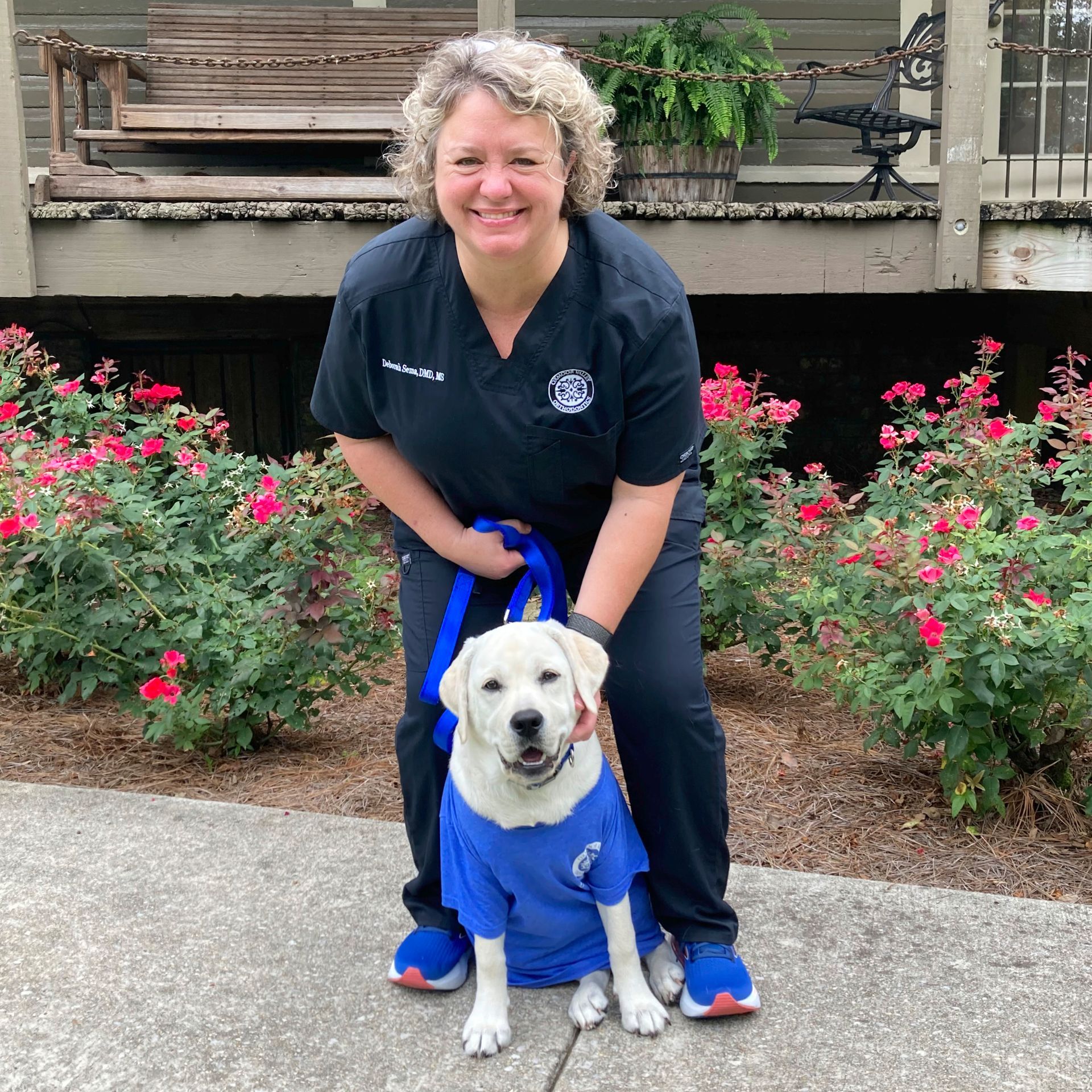 Dr. Sema is standing next to a dog wearing a blue shirt.