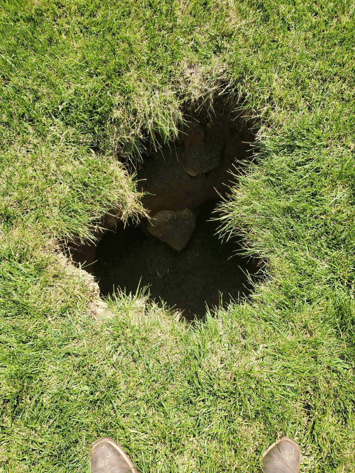 A person is standing next to a hole in the grass.